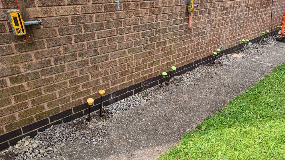 Geopolymer injection tubes capped along the side of a brick exterior residential home wall.
